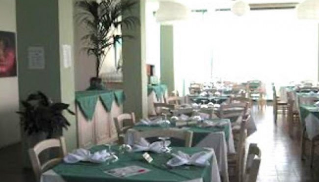 Sala da pranzo con tavoli apparecchiati, tovaglie verdi e piante decorative.