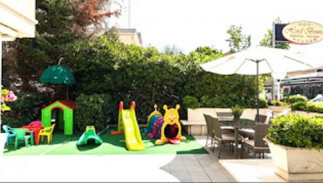 Area giochi per bambini all'aperto con scivolo, casetta e tavolino vicino a un tavolo esterno.