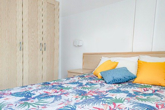 Camera da letto con armadio, copriletto floreale e cuscini colorati.