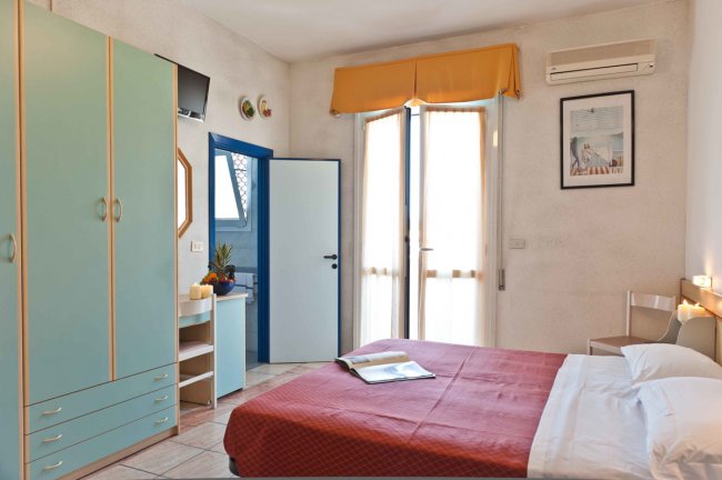 Camera da letto con letto matrimoniale, armadio verde, scrivania e accesso a un balcone.
