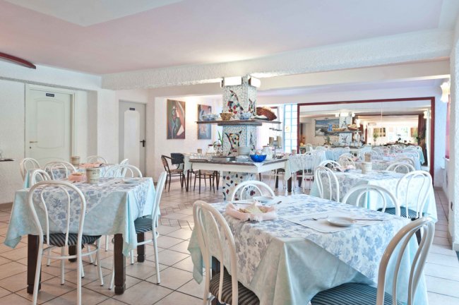 Sala da pranzo con tavoli apparecchiati, sedie bianche e decorazioni artistiche.