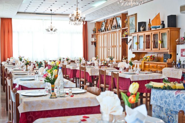 Sala da pranzo luminosa con tavoli apparecchiati e decorazioni floreali.