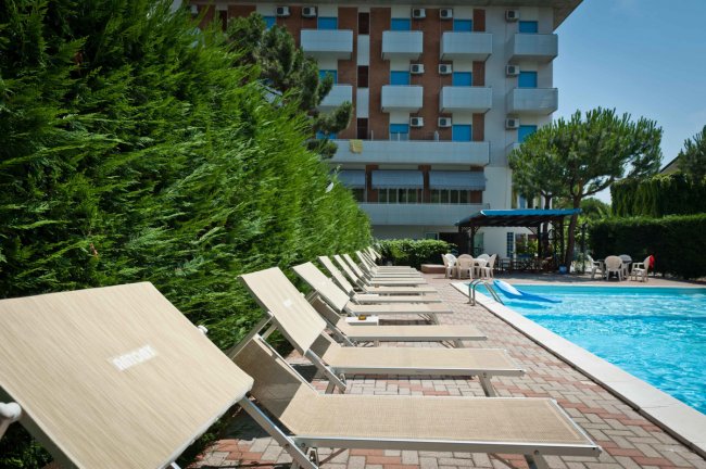 Lettini prendisole beige affiancano una piscina vicino a un edificio.