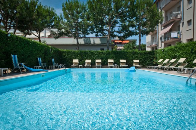 Piscina all'aperto circondata da lettini e alberi.