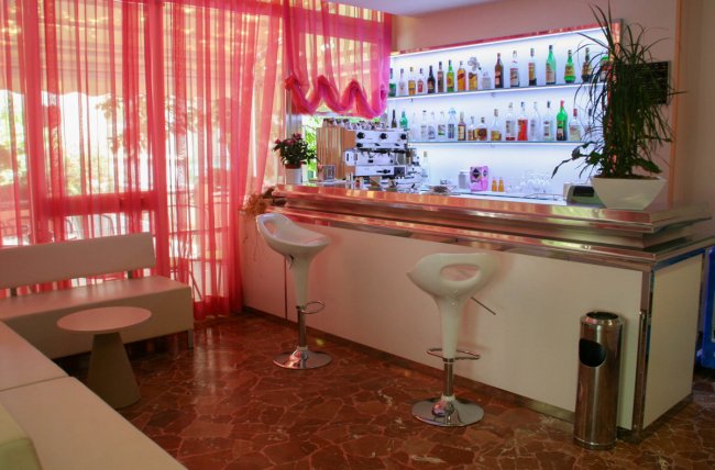 Bar con sgabelli bianchi e scaffali illuminati.