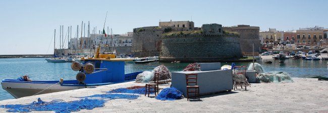 Porto con barche e reti da pesca, castello sullo sfondo.