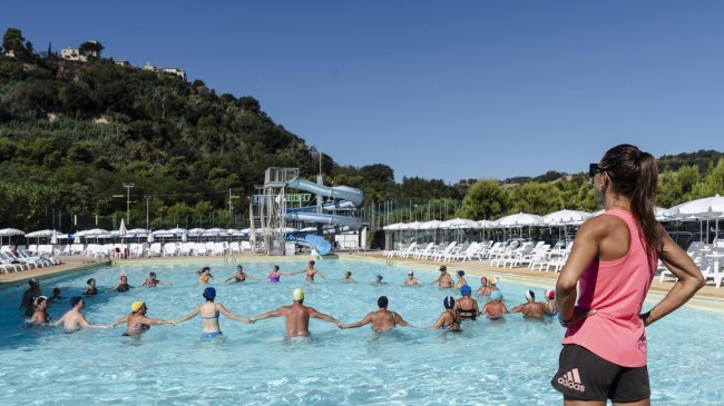 Persone in piscina con scivolo acquatico in lontananza.