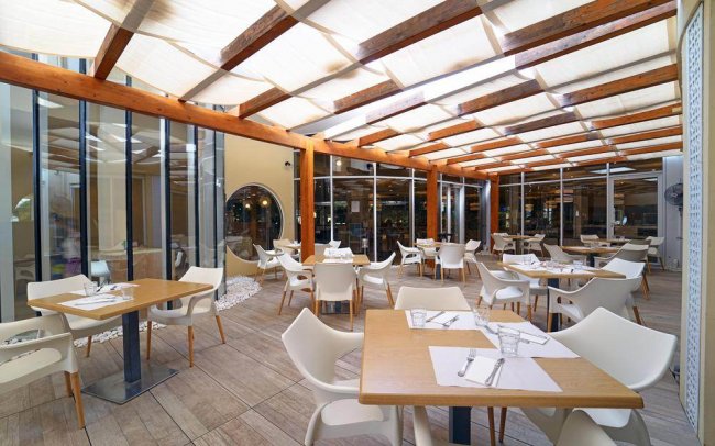 Area ristorante coperta con tavoli e sedie bianche.