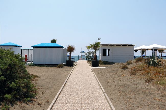 Sentiero tra dune di sabbia e capanni, vista mare.