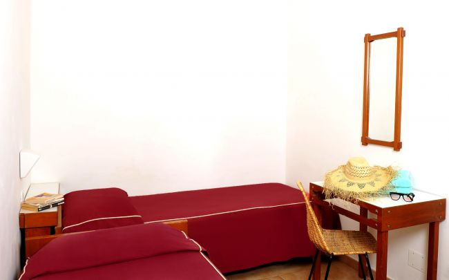 Camera da letto con due letti singoli e scrivania, cappello sulla sedia.