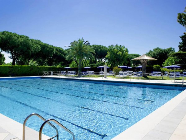 Piscina azzurra con lettini e ombrelloni intorno.