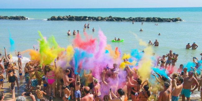 Spiaggia con persone che lanciano polveri colorate nell'aria.