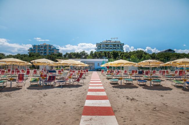 Spiaggia con ombrelloni gialli e lettini, hotel sullo sfondo.