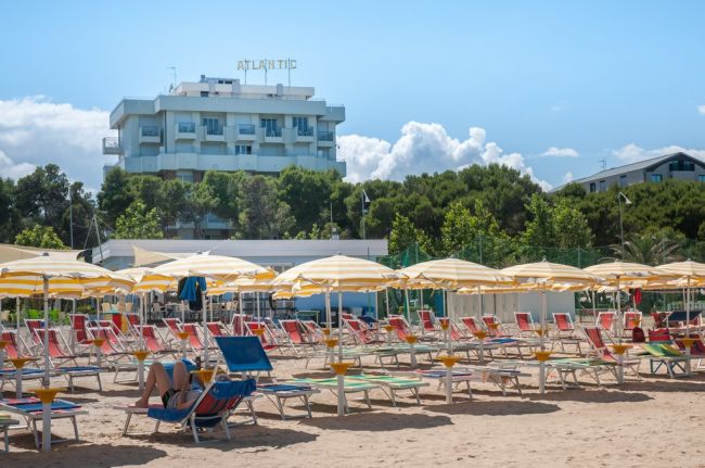 Spiaggia con lettini e ombrelloni, hotel bianco sullo sfondo.