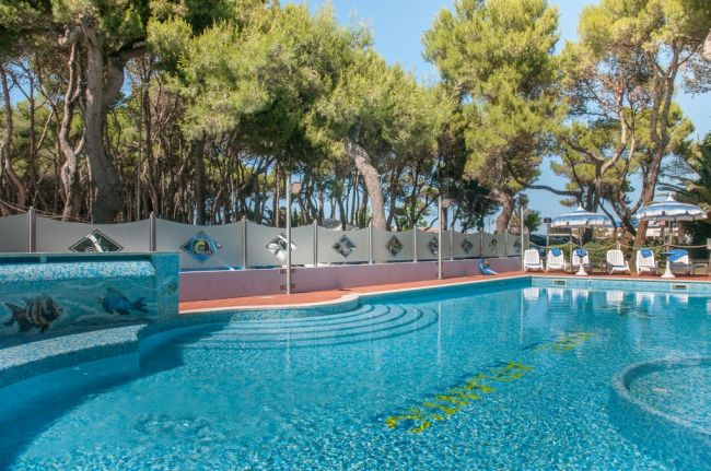 Piscina con mosaici blu e verde, immersa nel verde degli alberi.