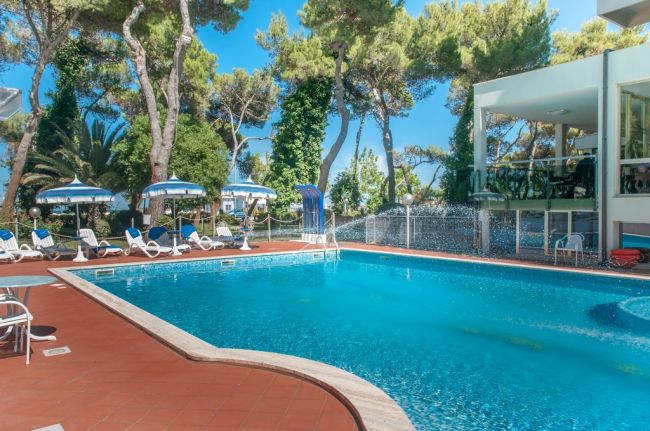 Piscina con sedie a sdraio e ombrelloni sotto gli alberi.