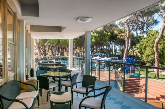 Veranda con tavoli e sedie vicino a un giardino con alberi.