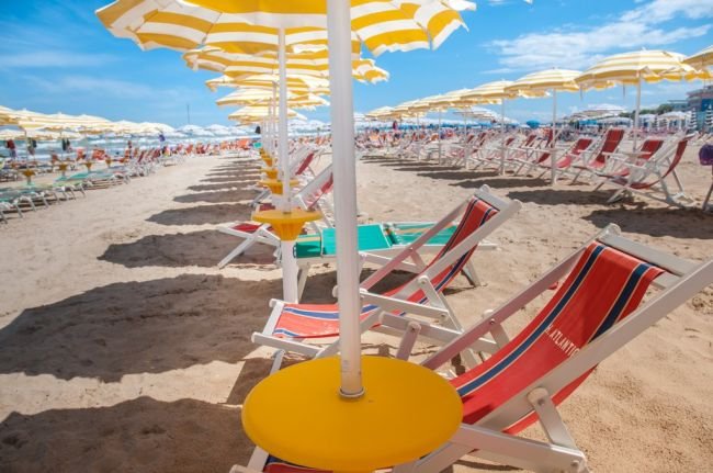 Spiaggia con sdraio rosse e ombrelloni gialli.