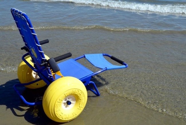 Sedia a rotelle da spiaggia blu con grandi ruote gialle sulla riva.