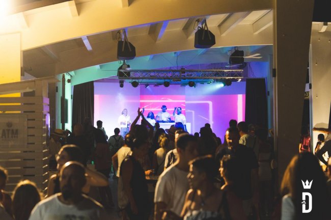 Persone che ballano in un locale con DJ sullo sfondo.