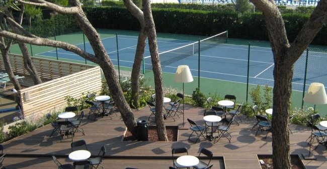 Area con tavoli e sedie vicino a un campo da tennis.