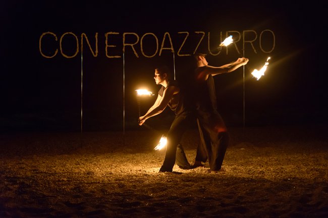 Giocolieri con fiamme si esibiscono di notte su una spiaggia.