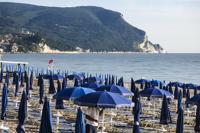 Spiaggia con lettini e ombrelloni blu vicino a un promontorio verde.