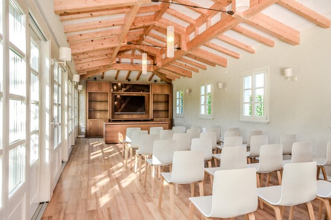 Una sala conferenze luminosa con sedie bianche e soffitto in legno.