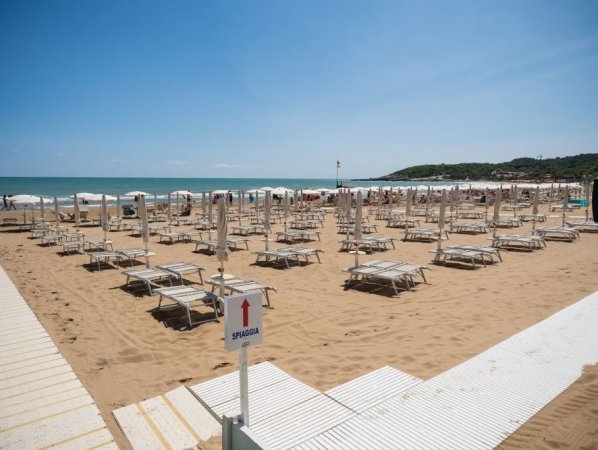 Spiaggia sabbiosa con lettini e ombrelloni bianchi sotto un cielo sereno.