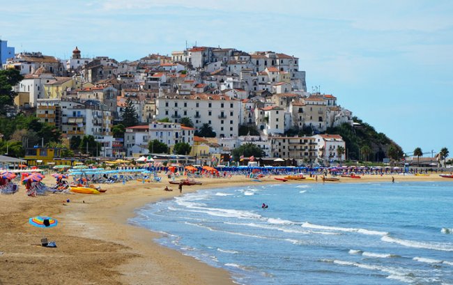 Spiaggia affollata con case bianche in lontananza.