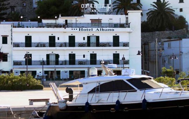 Un hotel bianco a tre piani vicino a una barca al molo.