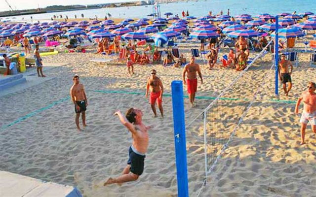 Persone giocano a pallavolo sulla spiaggia con ombrelloni colorati.