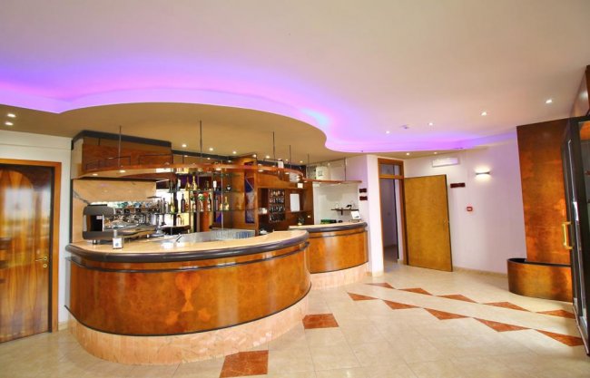 Bar con bancone curvo e illuminazione soffusa viola.