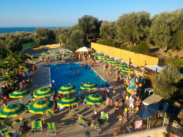 Piscina con ombrelloni verdi e gialli vicino al mare.