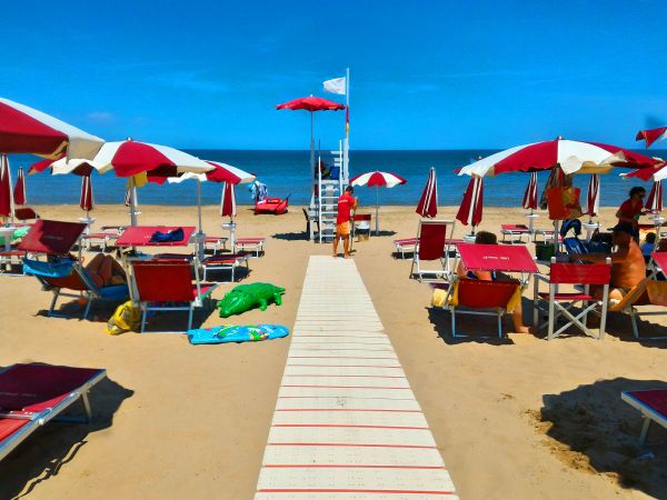 Spiaggia con sdraio e ombrelloni rossi e bianchi.