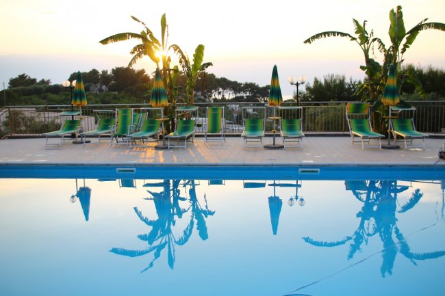 Piscina con ombrelloni verdi al tramonto.