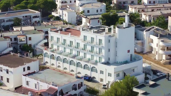 Un edificio bianco a più piani con balconi e tetto rosso su una strada cittadina.