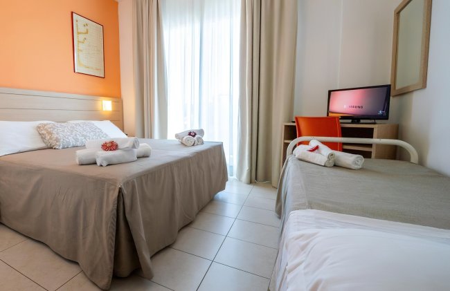 Una camera d'albergo con letto matrimoniale, letto singolo, TV e balcone.