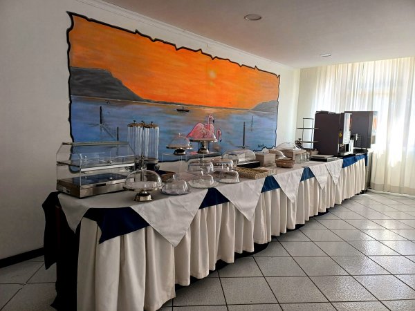 Buffet con tovaglie bianche e blu e un murale di tramonto sul mare.