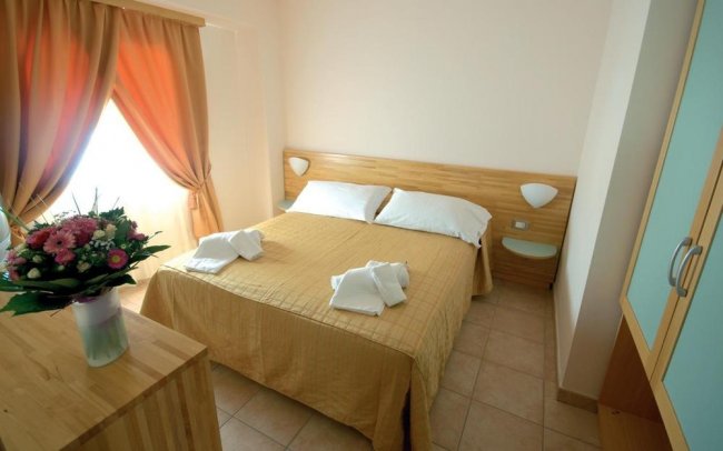 Camera d'albergo con letto matrimoniale e fiori sul comò.