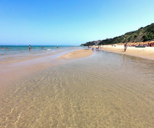 Spiaggia sabbiosa con poche persone in acqua.