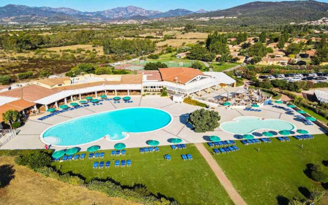 Piscina circondata da ombrelloni e prato verde.